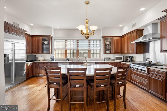 kitchen with an inviting chandelier, stainless steel appliances, wall chimney exhaust hood, and light hardwood / wood-style floors