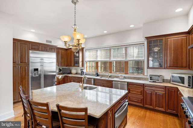 kitchen featuring light hardwood / wood-style floors, stainless steel appliances, an inviting chandelier, a kitchen island with sink, and sink