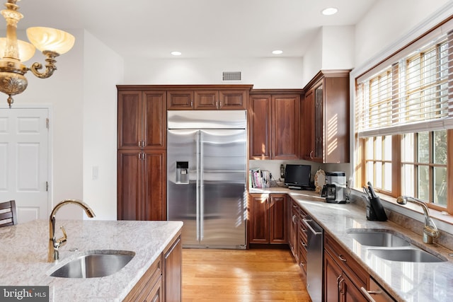 kitchen featuring light wood-type flooring, stainless steel appliances, sink, a chandelier, and light stone countertops