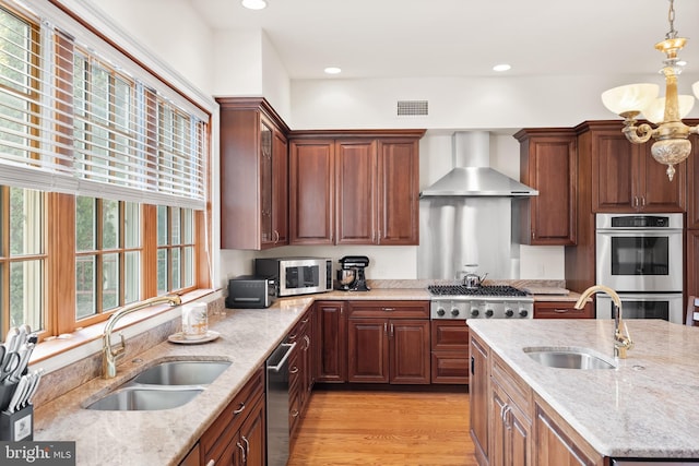 kitchen with pendant lighting, sink, wall chimney range hood, and light hardwood / wood-style floors