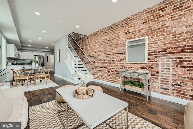 living room featuring brick wall and dark wood-type flooring