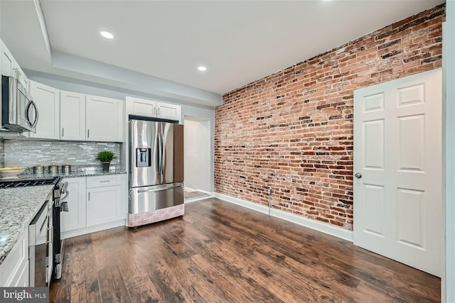 kitchen with brick wall, dark hardwood / wood-style floors, light stone counters, white cabinets, and appliances with stainless steel finishes