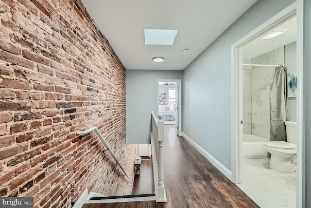 hallway featuring a skylight, brick wall, and dark wood-type flooring