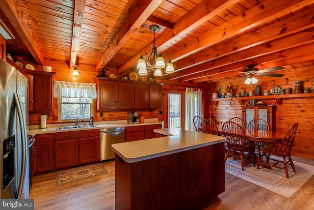 kitchen with sink, stainless steel appliances, pendant lighting, light hardwood / wood-style floors, and wooden walls