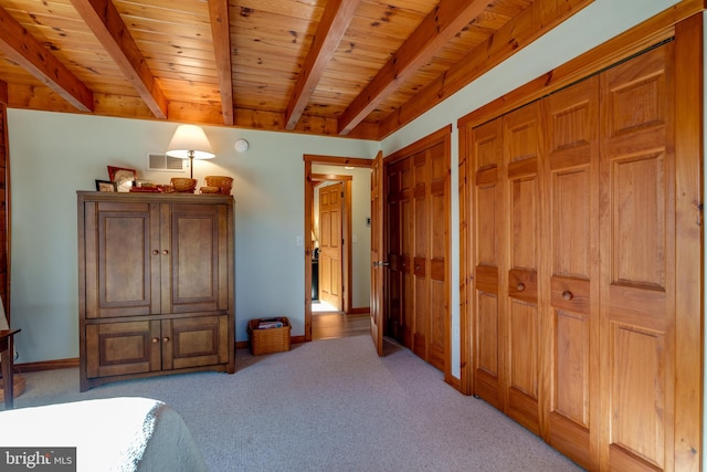 bedroom with wooden ceiling, beam ceiling, light colored carpet, and multiple closets