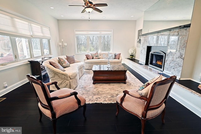 living room with ceiling fan, a high end fireplace, dark wood-type flooring, and a textured ceiling