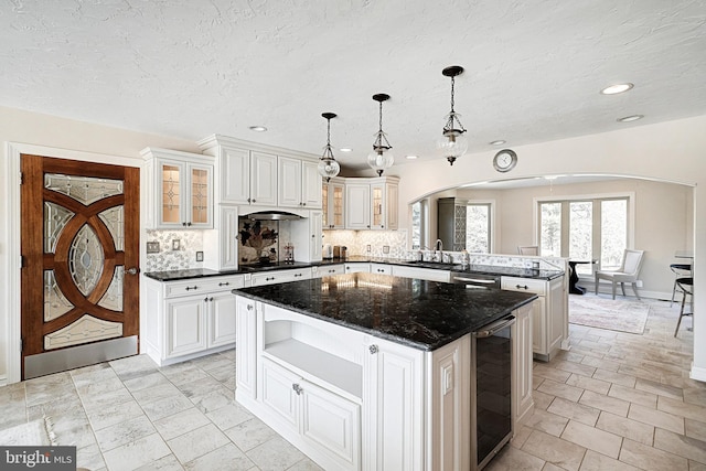 kitchen with a kitchen island, wine cooler, dark stone countertops, backsplash, and hanging light fixtures