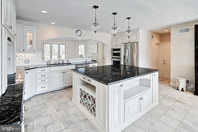 kitchen with a kitchen island, stainless steel appliances, dark stone countertops, decorative light fixtures, and sink