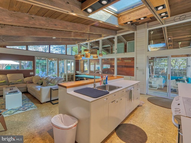 kitchen with stainless steel dishwasher, vaulted ceiling with skylight, sink, a center island with sink, and range