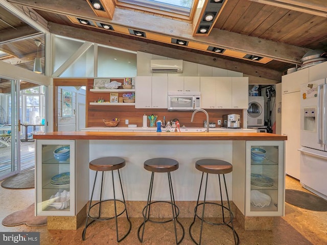 kitchen featuring white cabinetry, a wall mounted AC, lofted ceiling with skylight, white appliances, and a breakfast bar area