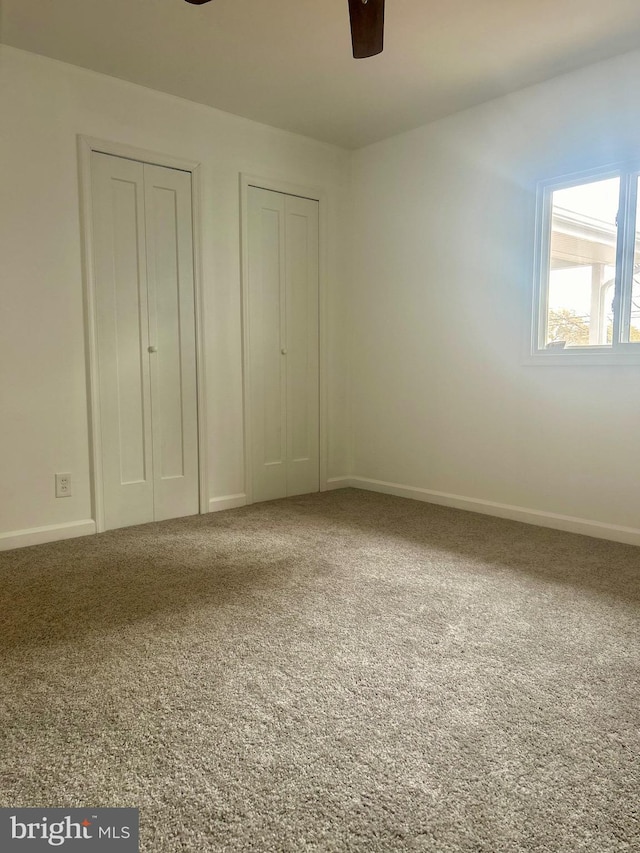 unfurnished bedroom with carpet floors, two closets, and ceiling fan