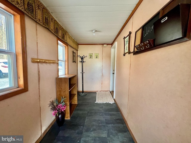 hallway featuring dark tile flooring, crown molding, and a healthy amount of sunlight