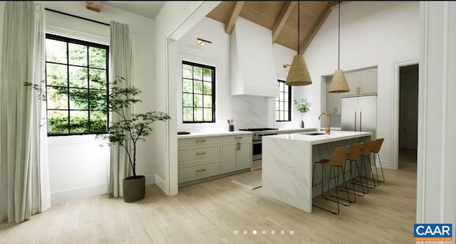 kitchen with a kitchen island with sink, sink, hanging light fixtures, light hardwood / wood-style floors, and high end stove