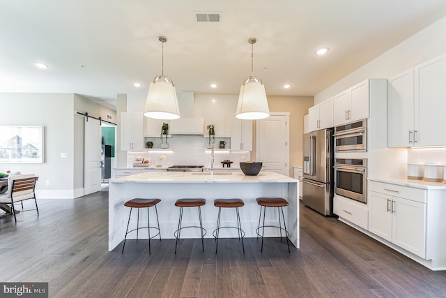 kitchen featuring pendant lighting, stainless steel appliances, a barn door, white cabinets, and dark hardwood / wood-style flooring