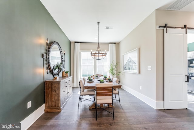 dining space featuring a barn door, dark hardwood / wood-style flooring, and an inviting chandelier