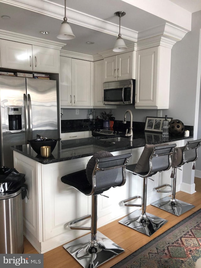 kitchen featuring white cabinetry, hanging light fixtures, wood-type flooring, and appliances with stainless steel finishes