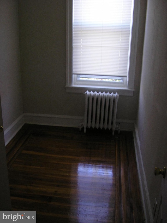 empty room with radiator heating unit and dark hardwood / wood-style flooring