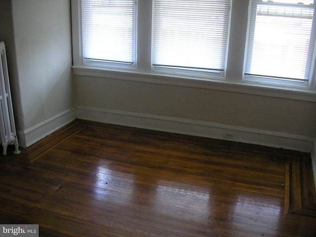 empty room featuring a healthy amount of sunlight, radiator, and dark wood-type flooring