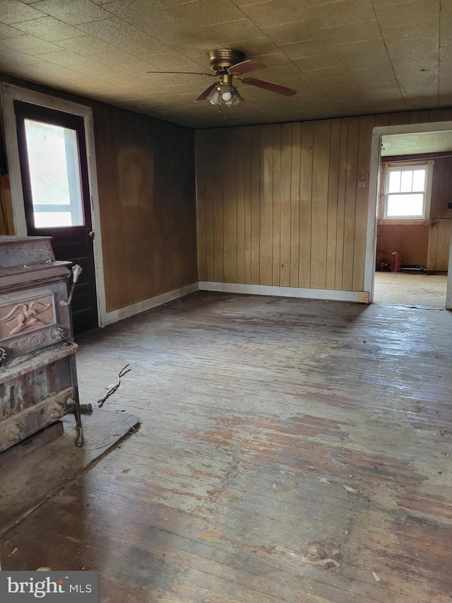 empty room with light hardwood / wood-style flooring, wood walls, a wood stove, and ceiling fan