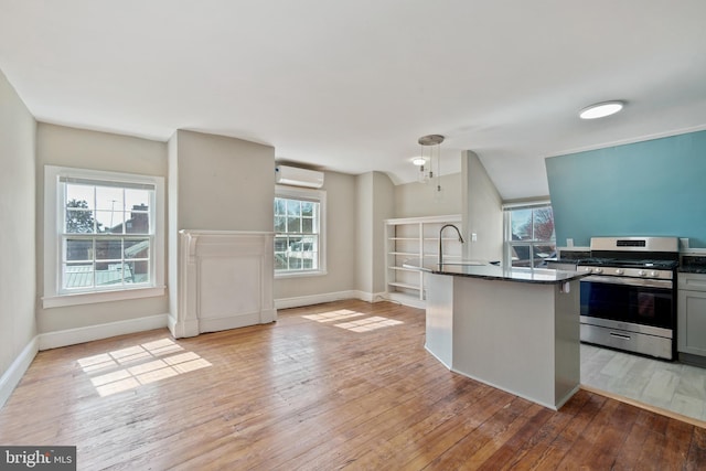 kitchen with stainless steel range with gas stovetop, sink, light wood-type flooring, an AC wall unit, and decorative light fixtures