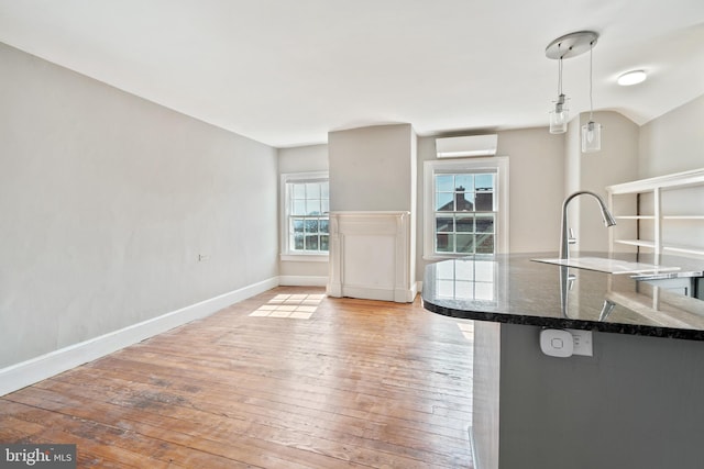 kitchen featuring a wall unit AC, light hardwood / wood-style floors, dark stone counters, and decorative light fixtures