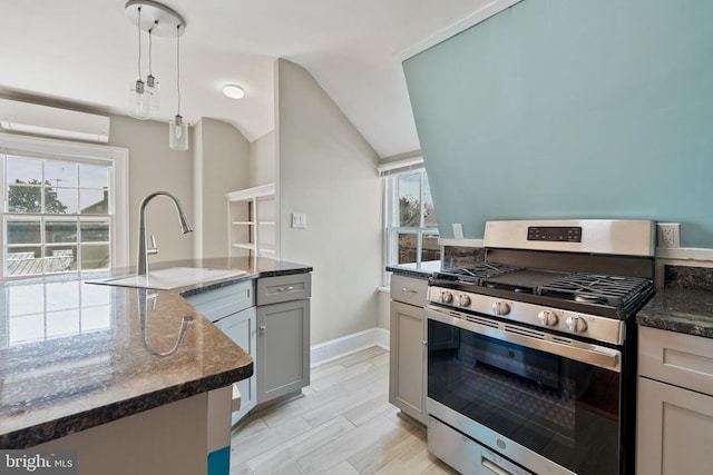 kitchen with decorative light fixtures, stainless steel range with gas stovetop, lofted ceiling, a wall unit AC, and sink