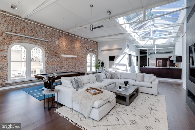 living room with pool table, hardwood / wood-style floors, a skylight, a high ceiling, and brick wall