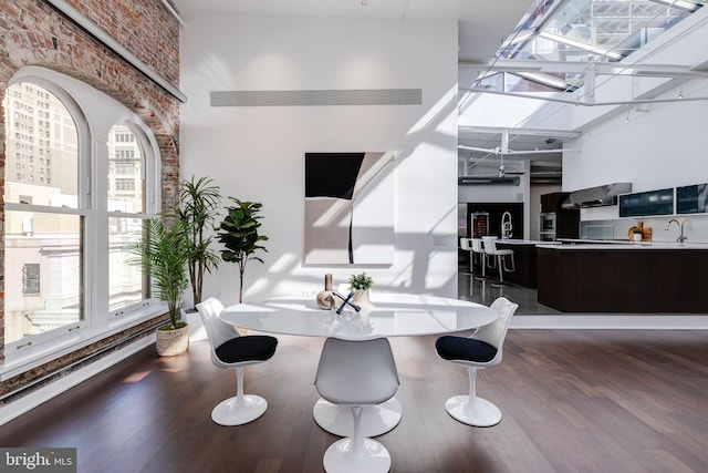 dining room featuring hardwood / wood-style flooring, sink, brick wall, and a high ceiling