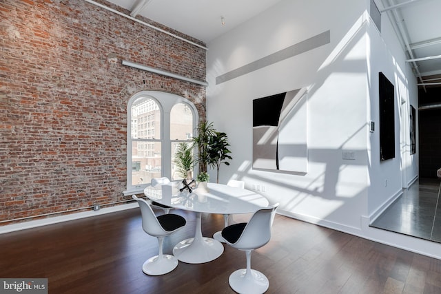 dining space with brick wall, dark wood-type flooring, and a high ceiling