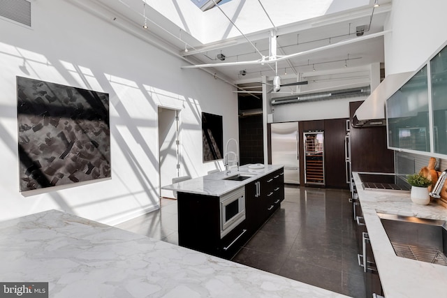 kitchen featuring a skylight, sink, a high ceiling, built in appliances, and a kitchen island with sink