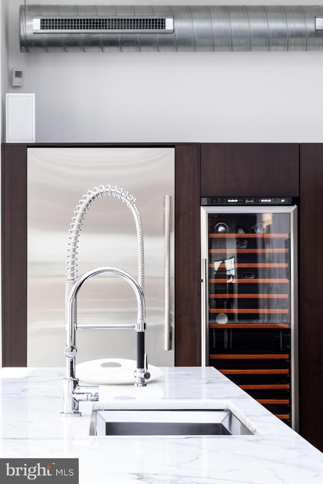 interior details featuring wine cooler, light stone counters, dark brown cabinets, and sink