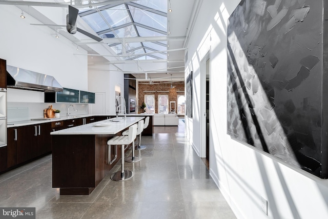 kitchen with exhaust hood, an island with sink, high vaulted ceiling, and a healthy amount of sunlight