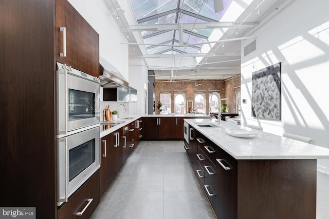 kitchen featuring pendant lighting, wall chimney exhaust hood, sink, and an island with sink