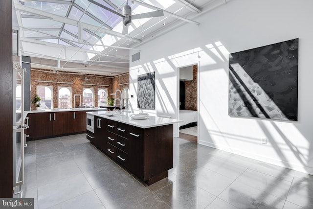 kitchen with a kitchen island with sink, dark brown cabinets, a skylight, high vaulted ceiling, and ceiling fan