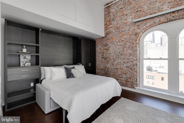 bedroom with brick wall, a towering ceiling, and dark hardwood / wood-style flooring