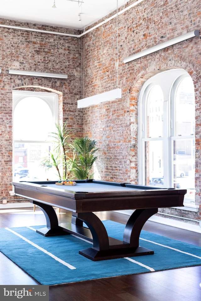 recreation room with brick wall, a towering ceiling, and hardwood / wood-style floors