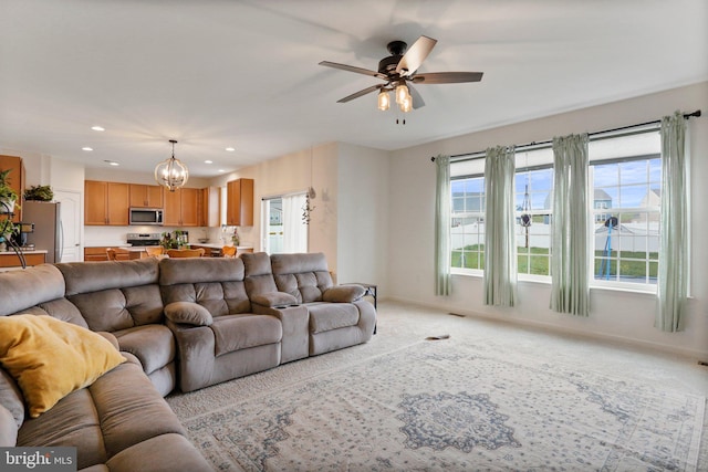 carpeted living room featuring ceiling fan with notable chandelier and a healthy amount of sunlight