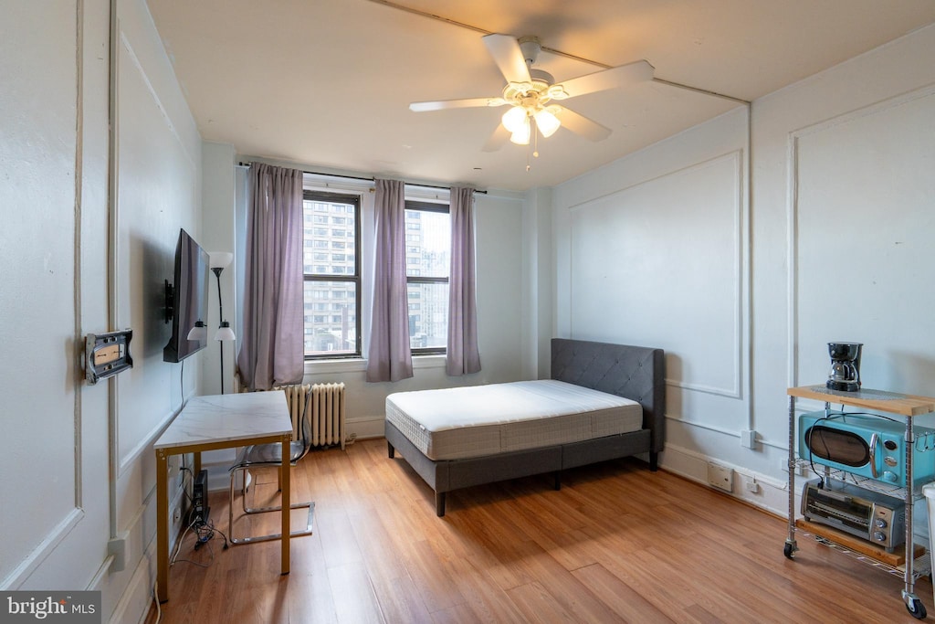 bedroom with radiator heating unit, ceiling fan, and light hardwood / wood-style flooring