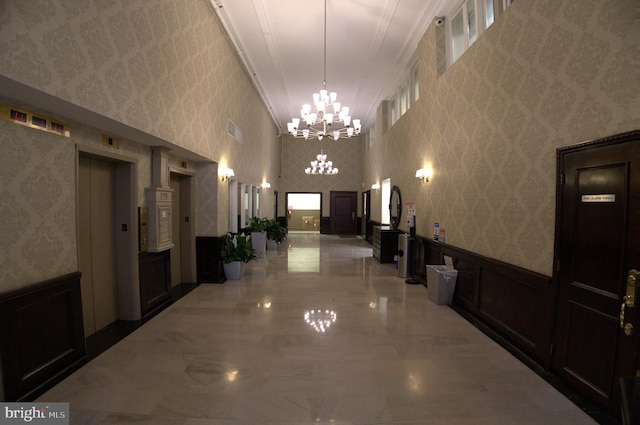 hall with elevator, a notable chandelier, light tile floors, a towering ceiling, and ornamental molding