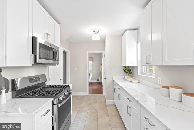 kitchen featuring appliances with stainless steel finishes, white cabinets, light tile floors, and light stone counters