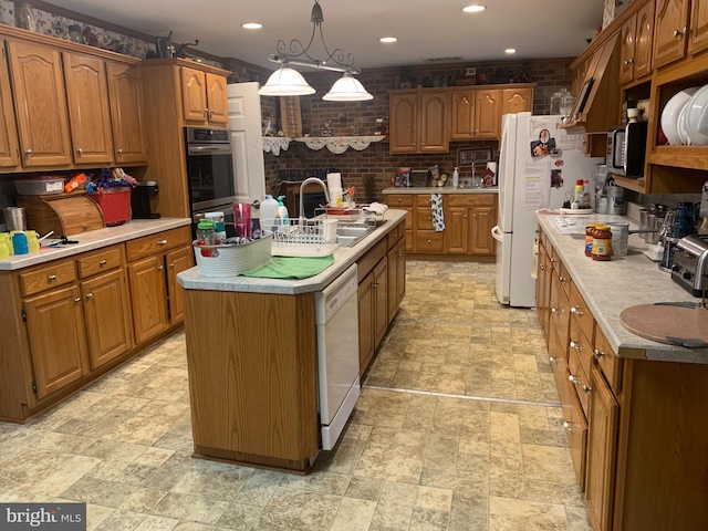 kitchen featuring brick wall, white appliances, pendant lighting, light tile floors, and a center island with sink