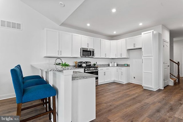 kitchen featuring dark wood-type flooring, stainless steel appliances, kitchen peninsula, light stone countertops, and a kitchen breakfast bar