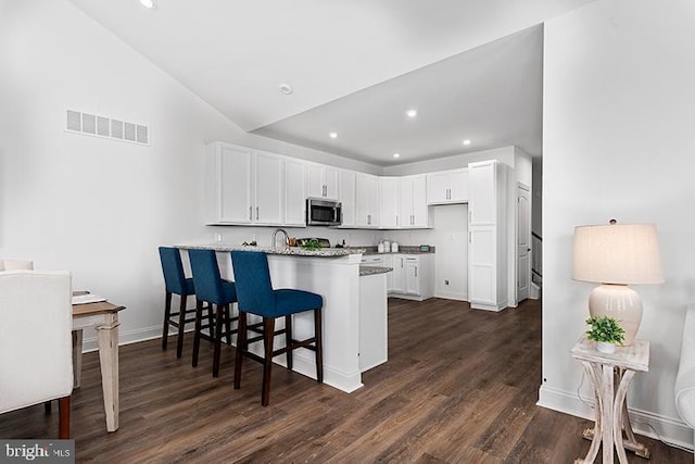 kitchen with white cabinets, kitchen peninsula, high vaulted ceiling, and dark wood-type flooring