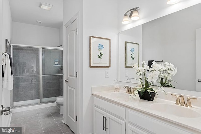 bathroom with toilet, large vanity, a shower with shower door, double sink, and tile floors