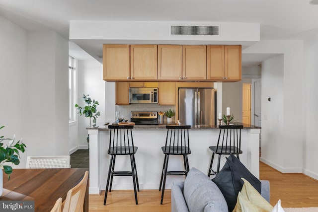 kitchen with dark stone counters, tasteful backsplash, a breakfast bar, stainless steel appliances, and light hardwood / wood-style flooring