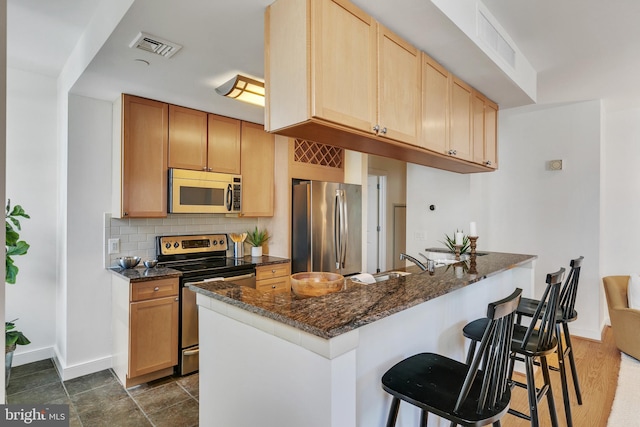 kitchen with dark hardwood / wood-style floors, kitchen peninsula, appliances with stainless steel finishes, dark stone countertops, and backsplash