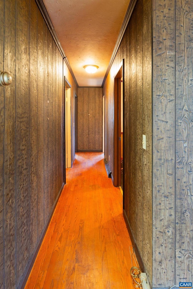 corridor with wooden walls, ornamental molding, and light wood-type flooring