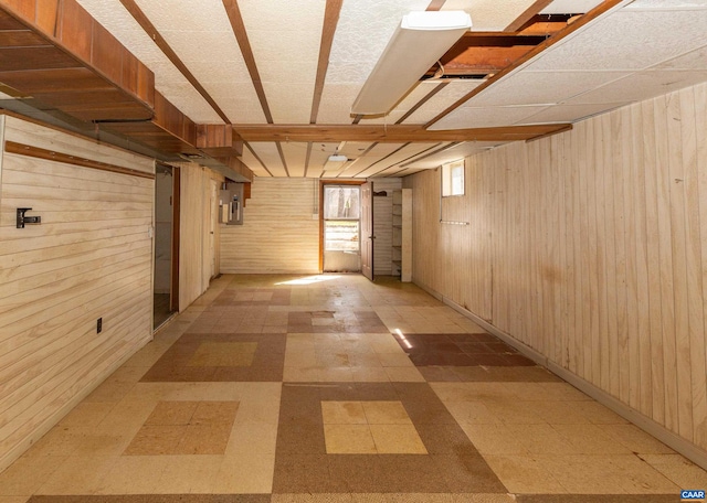 hallway featuring a paneled ceiling, wooden walls, and light tile floors