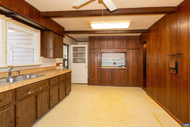 kitchen with ceiling fan, sink, light carpet, beam ceiling, and wooden walls