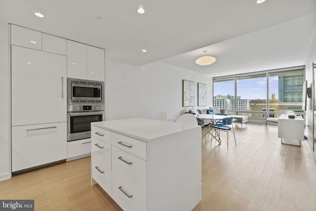 kitchen with light hardwood / wood-style flooring, appliances with stainless steel finishes, white cabinetry, a center island, and floor to ceiling windows